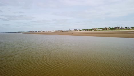 Cinematic-footage-of-a-young-man-running-and-walking-on-a-beach,-aerial