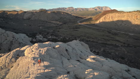 Female-Hiker-With-Backpack-and-Photo-Camera-Climbing-on-Rocky-Hill-in-Desert-Landscape,-Slow-Motion