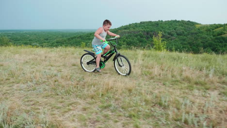 a little smiling boy comes down from a hill on a bicycle