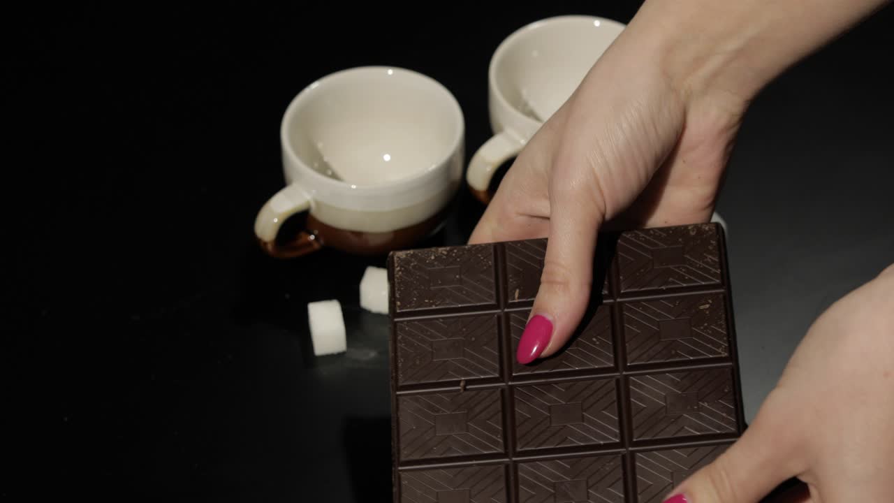 una mujer rompe una barra de chocolate negro. un primer plano de los dedos de una mujer.