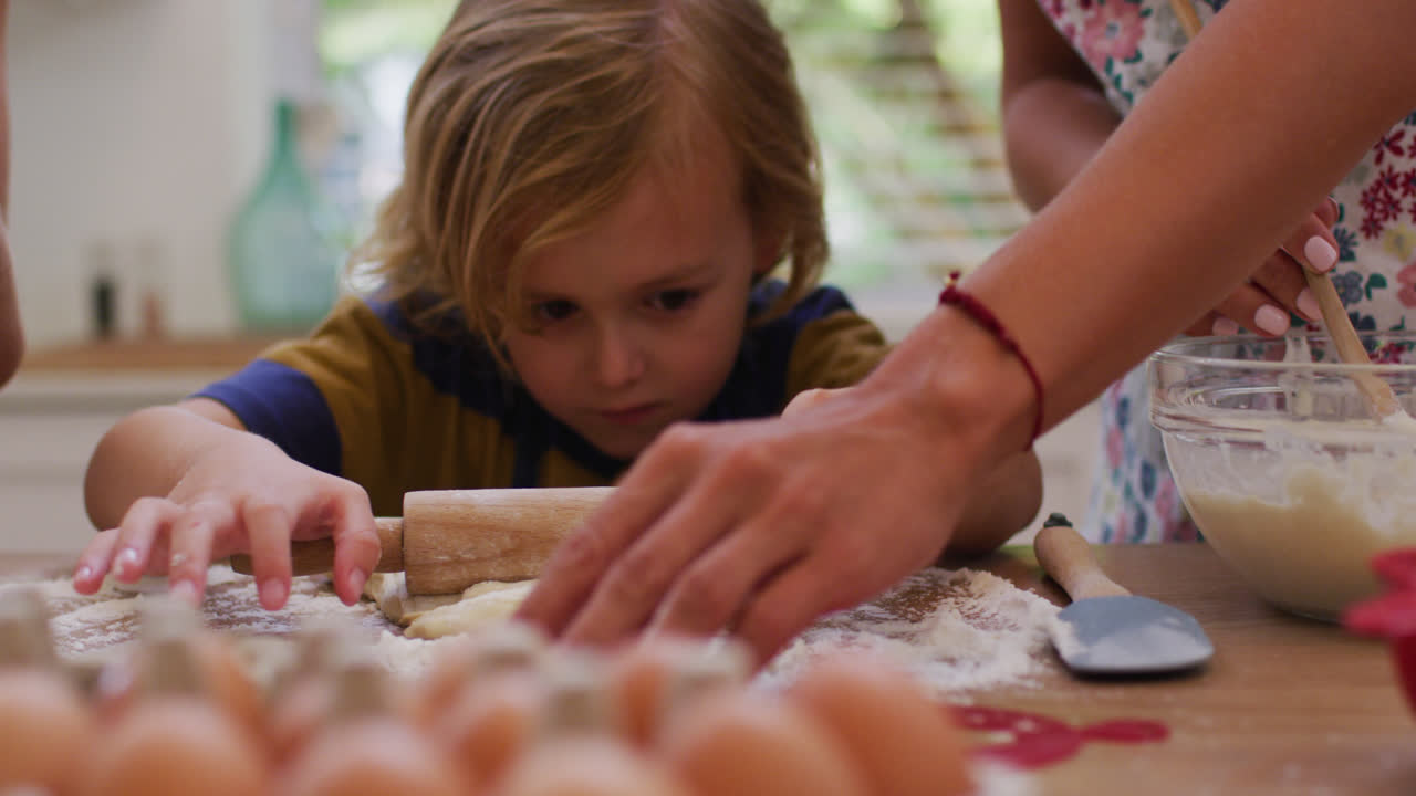 Caucasian son in kitchen rolling dough with mother and sister wearing aprons, baking together