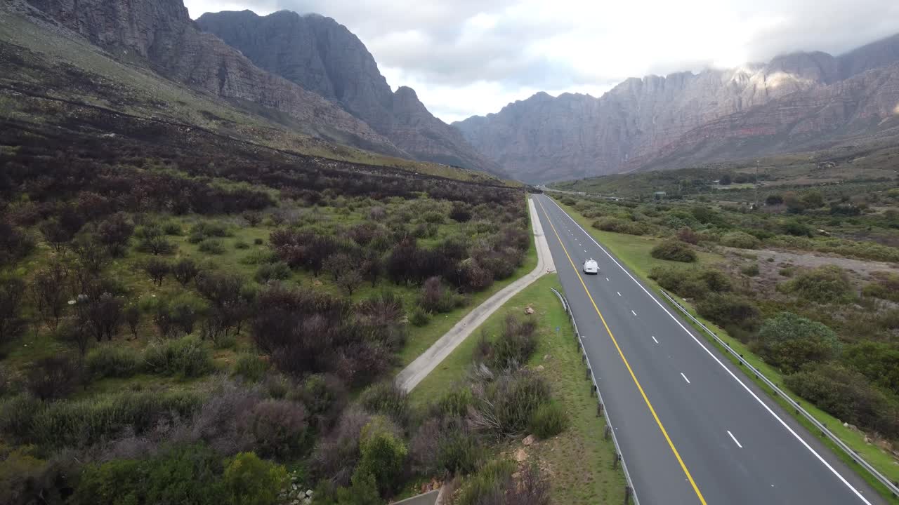 Aerial view of a drone shot following a white van driving down a highway all alone and seeing the mountain region around it