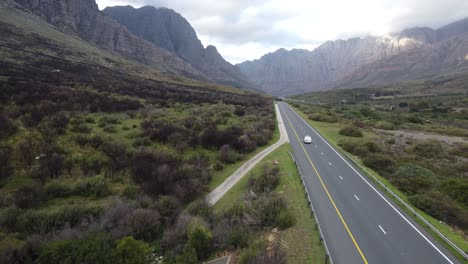 aerial view of a drone shot following a white van driving down a highway all alone and seeing the mountain region around it