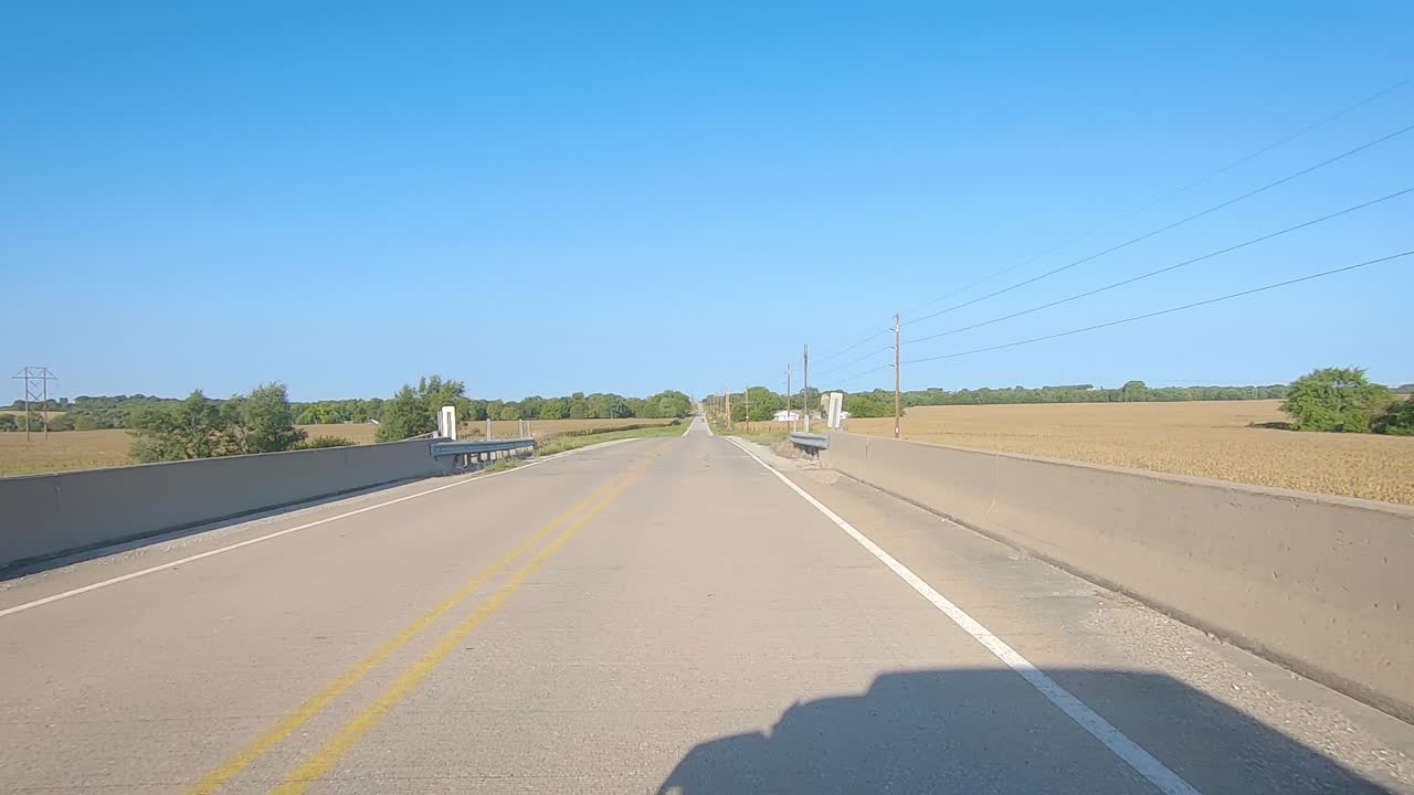 화창한 초가을날 아이오와 시골의 성숙한 옥수수 밭과 농장 구내를 지나 다리 위를 운전하는 포브