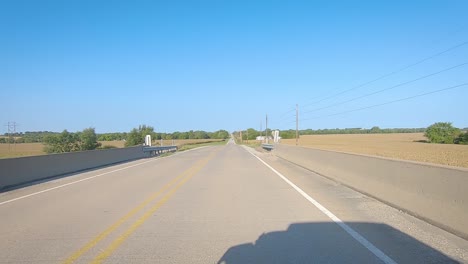 pov driving over a bridge and past mature corn fields and farmyards in rural iowa on a sunny early autumn day