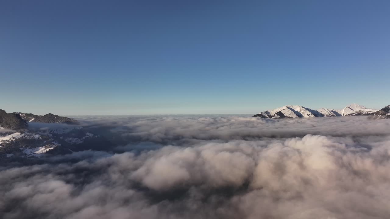 Stunning aerial drone view above Klöntalersee, Klöntal, Glarus, Switzerland, snowy peaks rising above clouds in serene alpine landscape.