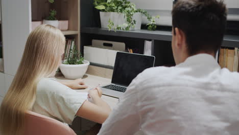 The-older-brother-helps-his-sister-with-homework,-their-cat-is-sitting-next-to-him.-Study-at-home.-Back-view