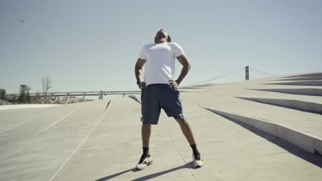 Smiling-young-man-stretching-arm-during-sunny-day.