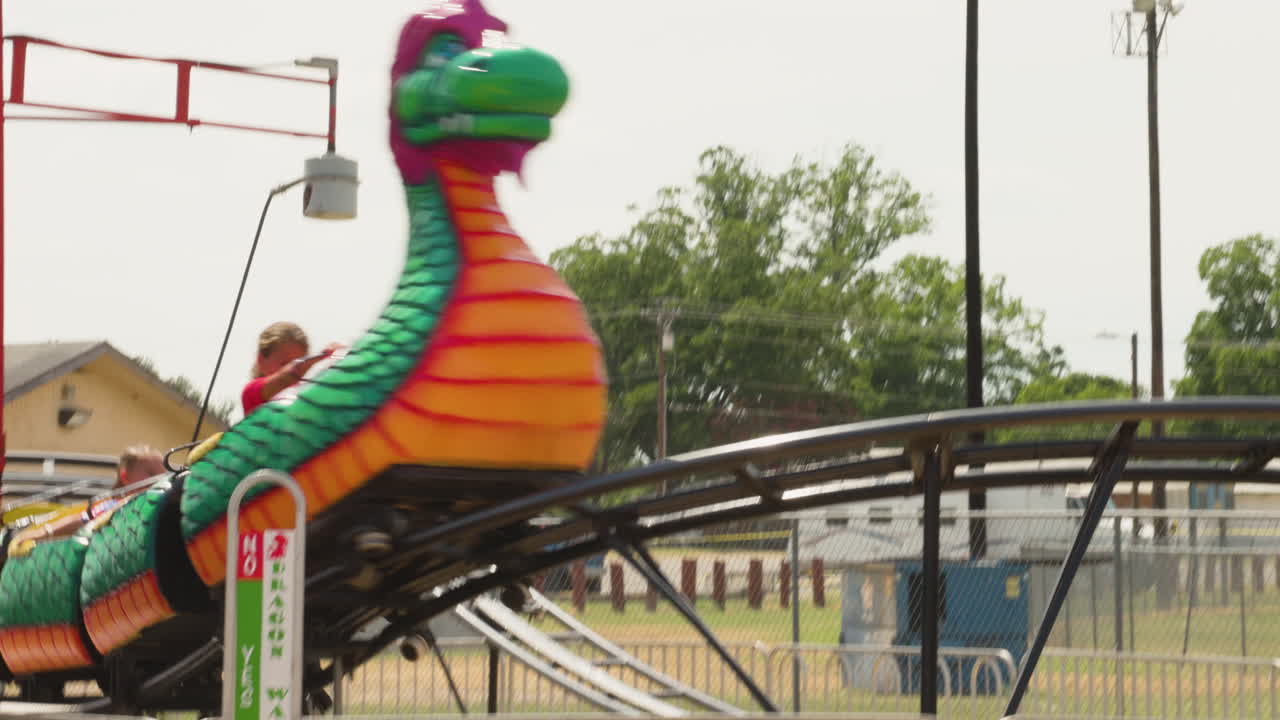 A carnival roller coaster for young kids moving along its tracks, capturing the vibrant atmosphere of the fair with excited children enjoying the ride.