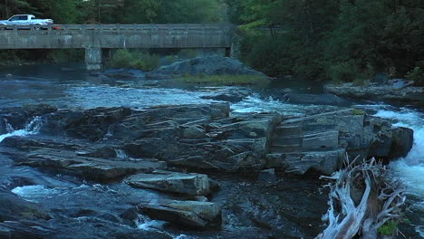 aerial drone shot in slow motion emerging from a thick mist over the dark waterfalls at big wilson falls and a bridge with cars and trucks in the maine wilderness