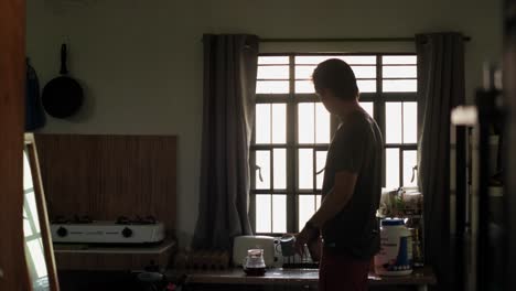 young man shaking protein shake bottle and drinking by sunlit apartment window - wide static shot