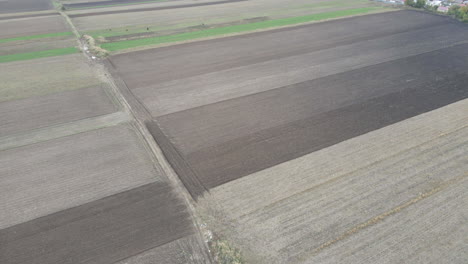 Low-altitude-flight-over-brown-and-green-farmland-drone-aerial-with-houses-behind