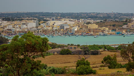 toma de alto ángulo sobre la pintoresca ciudad a lo largo de la costa, frente a la costa de marsaxlokk, malta con barcos de pesca movimiento en el lapso de tiempo