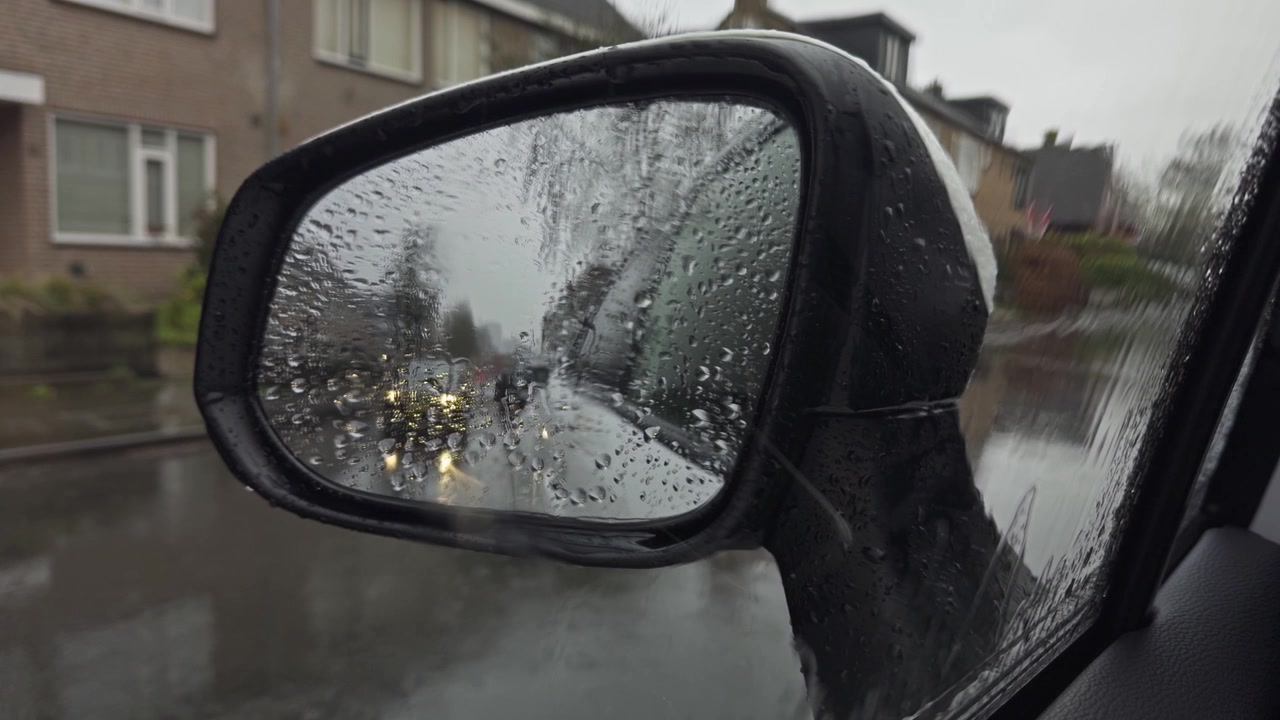Gocce di pioggia su uno specchietto laterale dell'auto in una giornata cupa e umida con un ciclista sullo sfondo