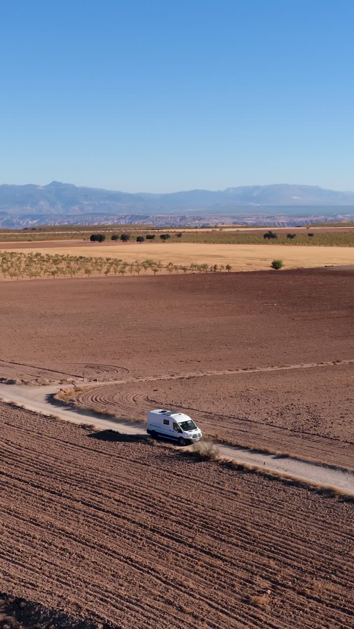 Vista aérea de una furgoneta camper conduciendo por un camino de tierra a través de campos áridos