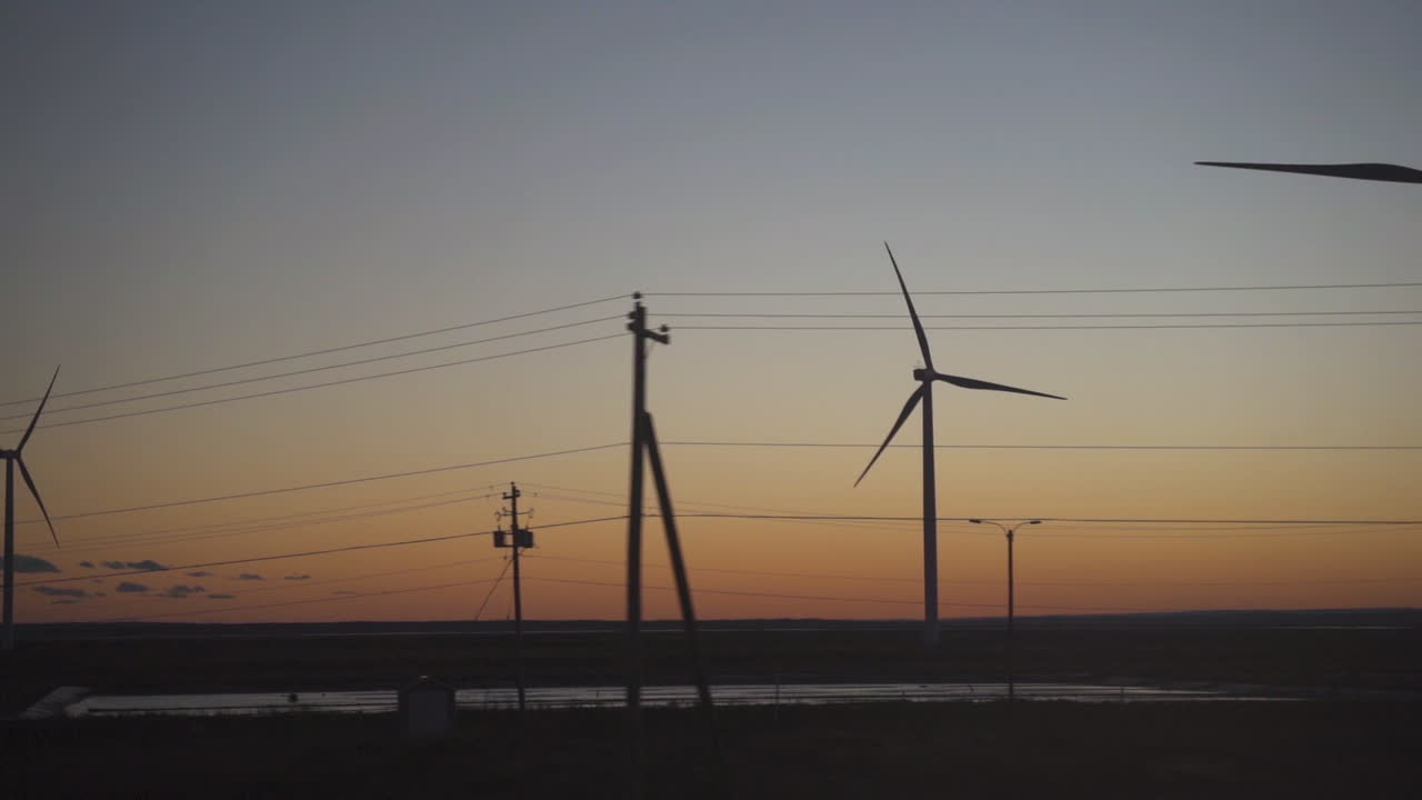 Pan right to left clean green energy wind turbines at sunset in field