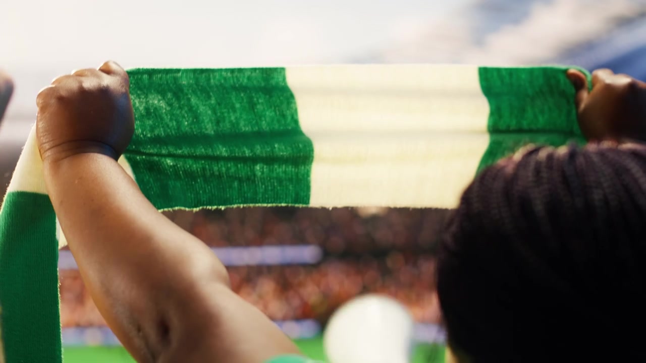 Primo piano di una donna allo stadio che solleva una sciarpa con i colori della squadra.
