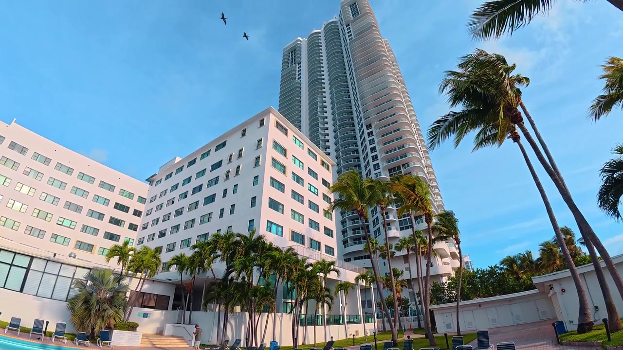 Piscina esterna in un resort alberghiero a Miami Beach. Acqua blu in piscina con lettini su un patio in mattoni vicino a edifici bianchi sotto un cielo sereno.