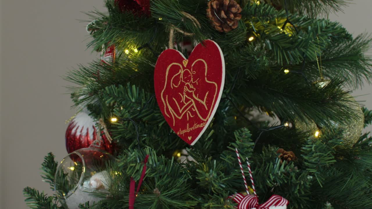 heart shaped ornament of parents and baby on christmas tree with lights