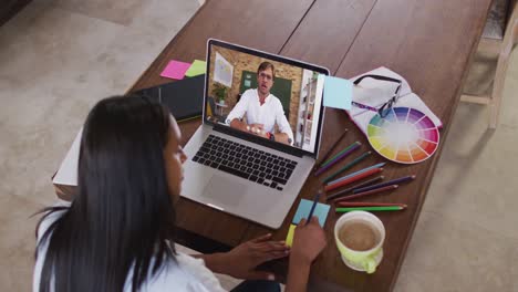 Caucasian-female-student-using-laptop-on-video-call-with-male-teacher,-making-notes