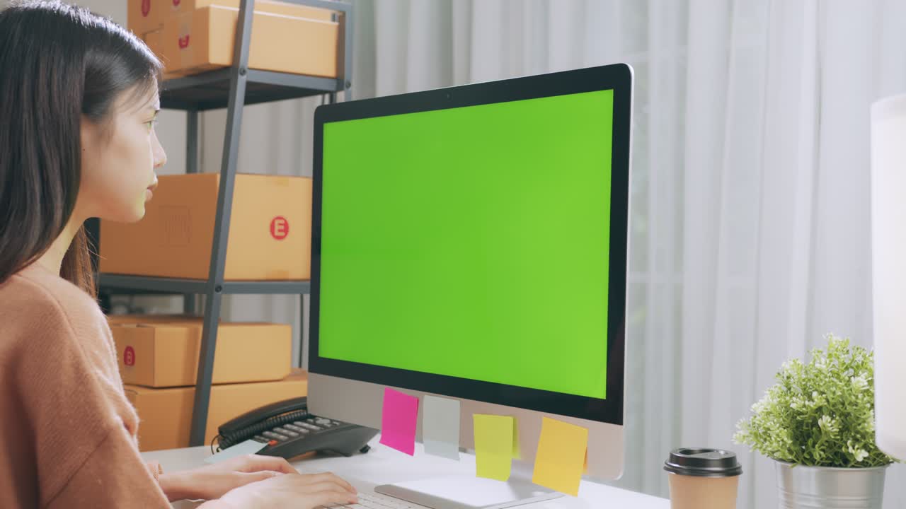 Startup small business, Young Asian woman checking online order on computer with green screen. and packing boxes for products to send to customers.
