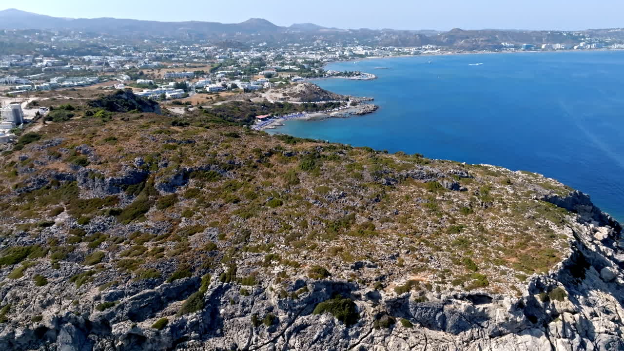 Aerial view tilting over a cliff, revealing the Faliraki coastline, in sunny Rhodes