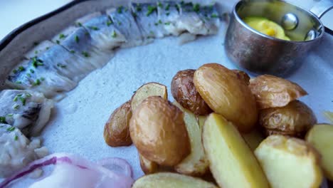 a plate of swedish herring with fried potatoes and red onion