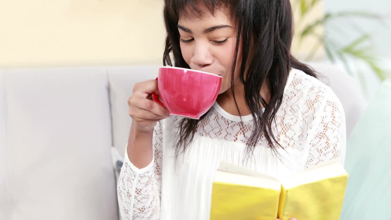 소파 위에 컵과 책을 들고 있는 여자