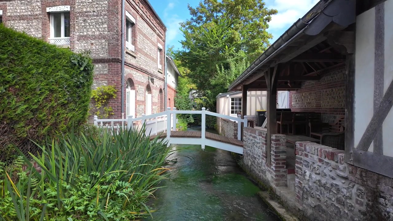 Riprese al rallentatore di un piccolo ponte pedonale bianco che attraversa il fiume Veules tra edifici tradizionali a Veules-les-Roses, Normandia, Francia