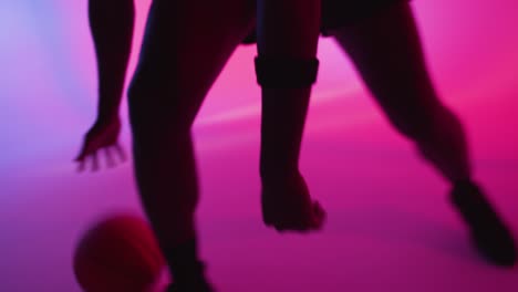 silueta de estudio de cerca de un jugador de baloncesto masculino driblando y rebotando la pelota contra un fondo iluminado de color rosa 1