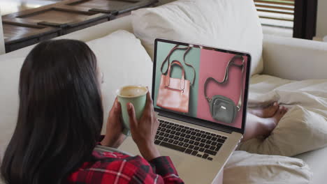 mischrassige frau auf der couch mit kaffee, mit laptop zum online-shopping, slowmotion