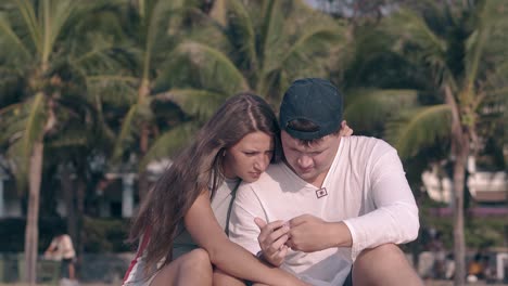 una joven pareja en el vestido de verano se sienta y mira el teléfono inteligente