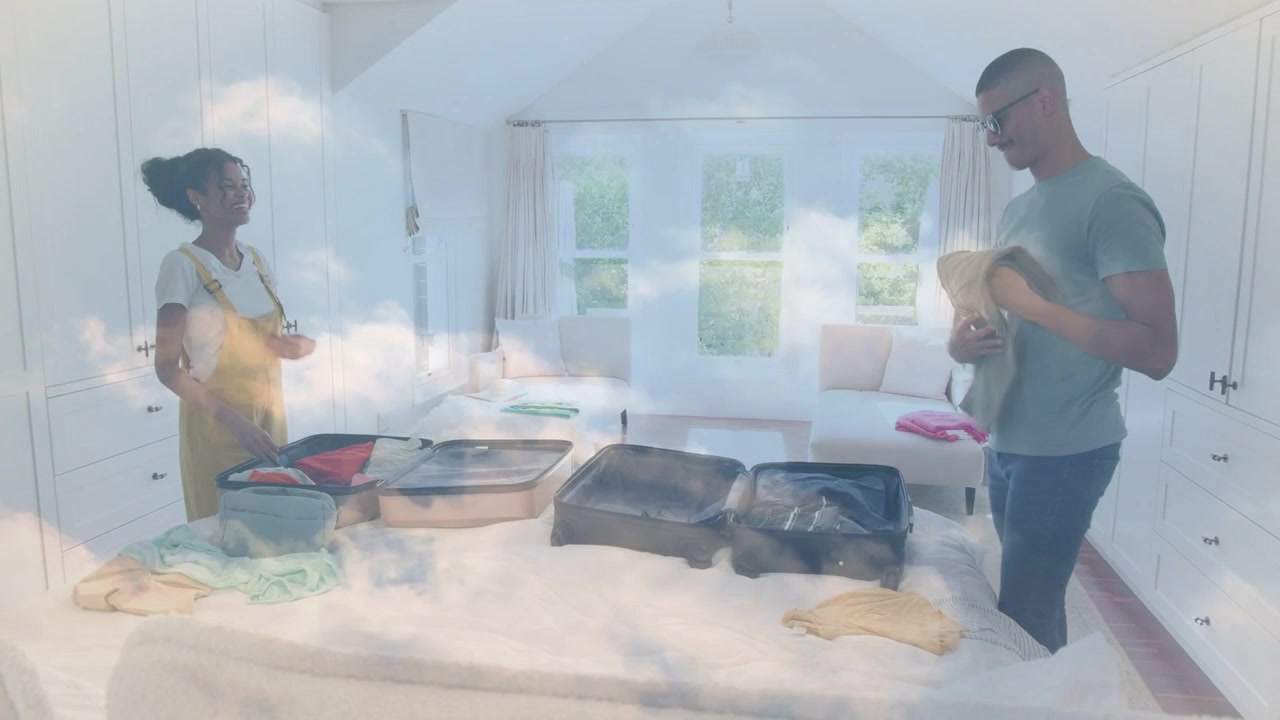 Man kneeling, woman packing cases on bed, holding glasses, cloud haze drifting across pair for trip