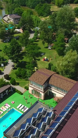 The territory of modern spa resort outside the city. Swimming pool with people resting around and having fun activities. Aerial perspective. Vertical video