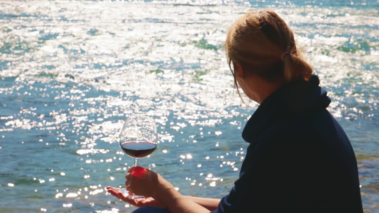 Woman enjoying a glass of red wine by a river