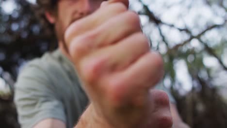 bearded caucasian male survivalist tying paracord to branch to make a fire bow at camp in wilderness