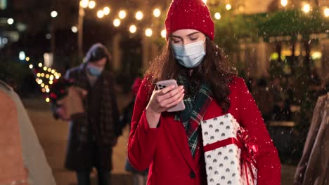 retrato de una joven hermosa y feliz escribiendo en un smartphone y caminando por la calle mientras nieva en navidad