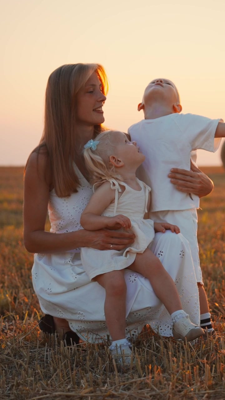 Mutter und zwei kleine Kinder sitzen bei Sonnenuntergang auf einem Feld