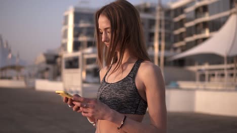 aspecto impresionante de una chica de cabello largo en un sujetador deportivo. páginas de desplazamiento en el teléfono móvil. piel clara. el viento agita fácilmente el cabello. fondo borroso