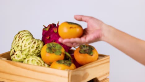 hand picking persimmon from wooden crate