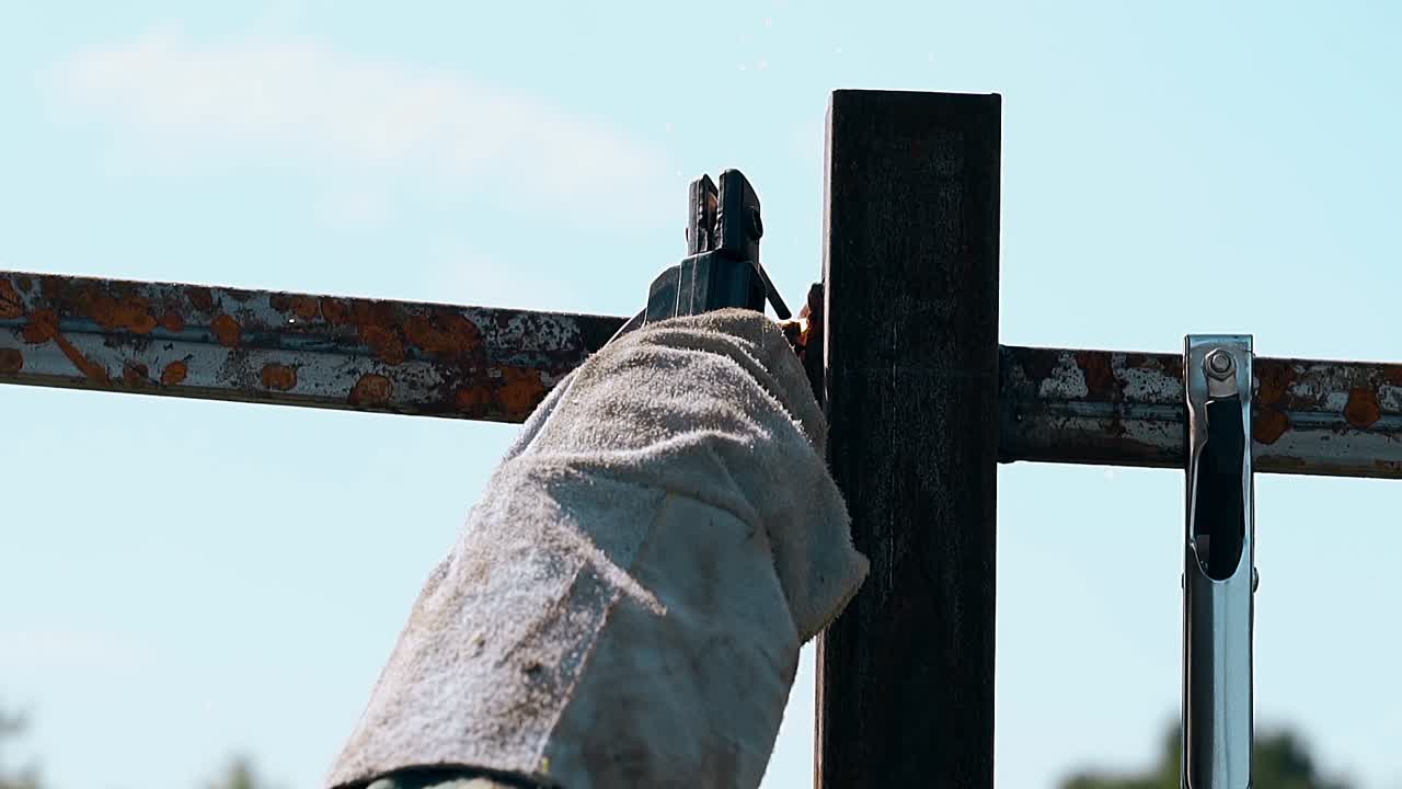 특수 장갑을 입은 클로즈업 용접기가 울타리의 사체를 고정합니다.