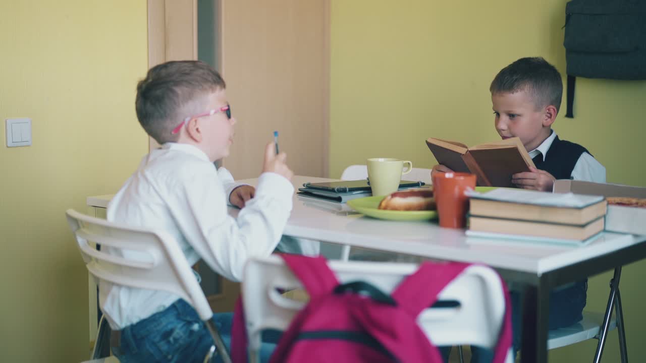 간식 과 교과서 를 가진 학교 소년 들 이 식당 의 테이블 에 앉아 있다