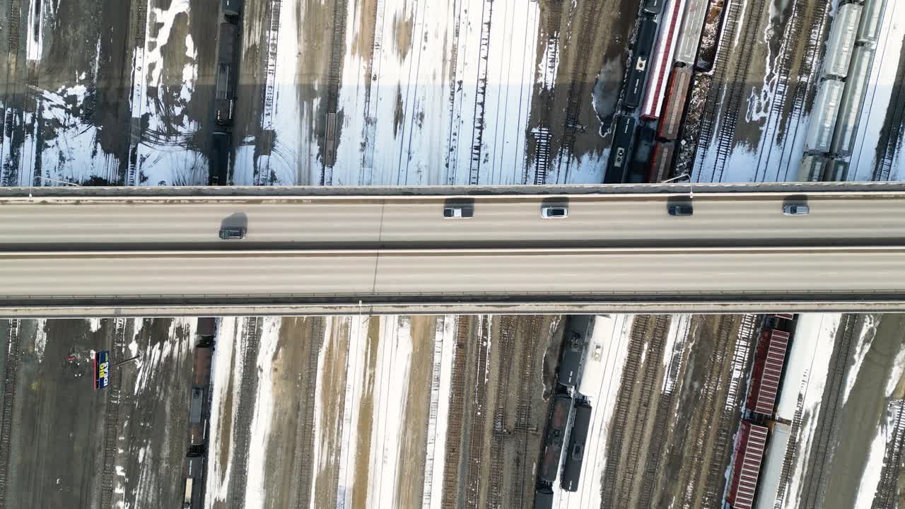 Pengambilan gambar drone statis dari atas sebuah jembatan dengan mobil-mobil yang melaju di atas rel kereta api