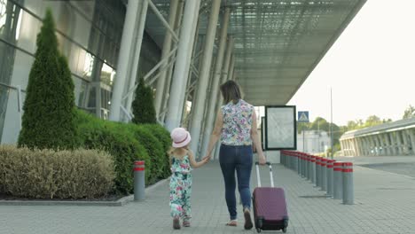 mother and daughter walking to airport. woman carrying suitcase bag. child and mom vacation. rear