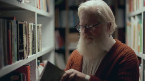 senior man with white beard choosing and reading book in library