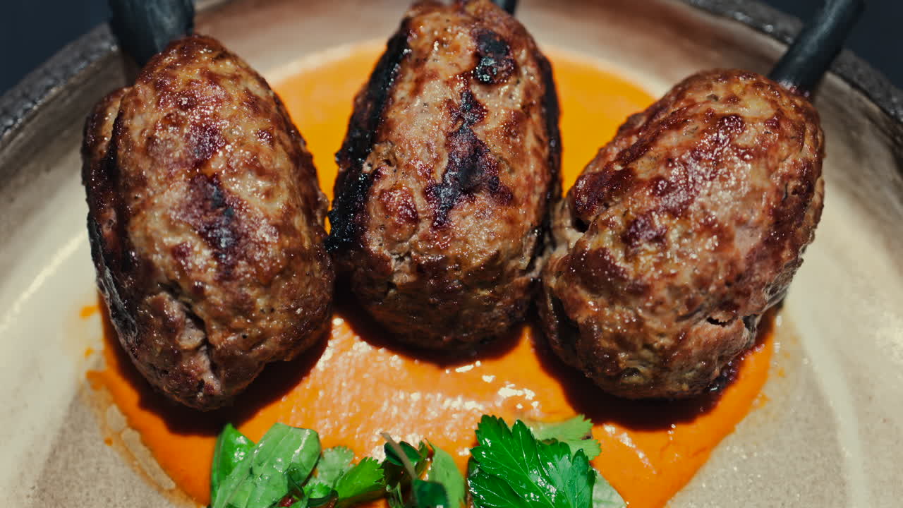 Three grilled meat skewers on charcoal sticks served on a plate with an orange sauce