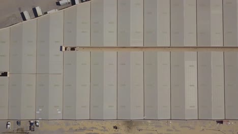 vista vertical de pájaro alejar la revelación de muchos almacenes de instalaciones de almacenamiento uno al lado del otro en el desierto con camiones