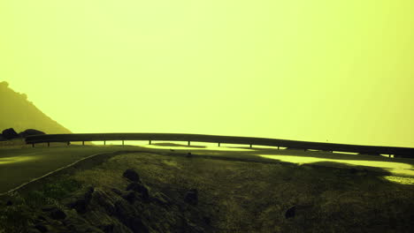 curved road along rocky terrain with bright yellow sky at sunset