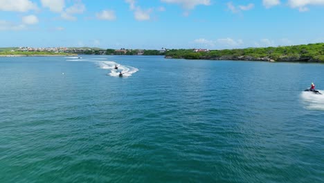 aerial push in as jet skis approach from front and behind driving up open channel in caribbean