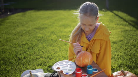 A-child-paints-a-pumpkin,-prepares-decorations-for-Halloween.-Sits-on-the-lawn-in-the-backyard-of-the-house